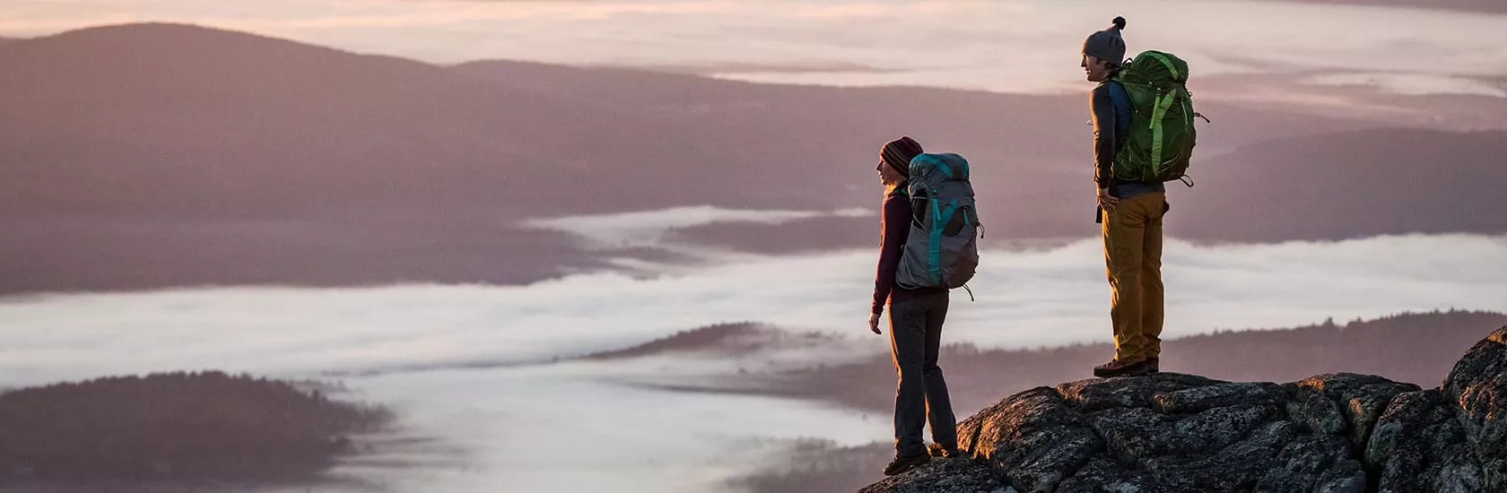 Two hikers overlooking a vast view. Wearing Osprey packs